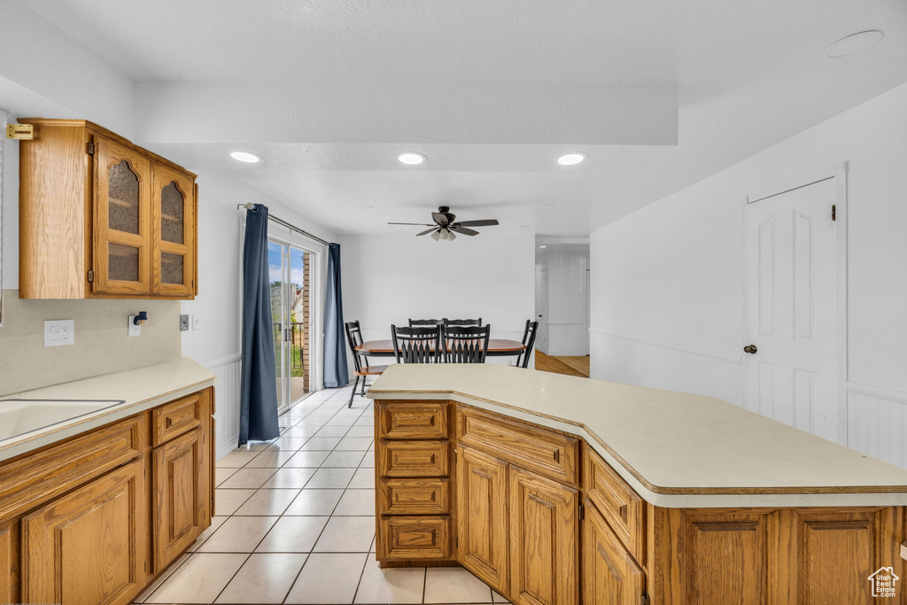 Kitchen featuring ceiling fan, light countertops, brown cabinetry, glass insert cabinets, and recessed lighting