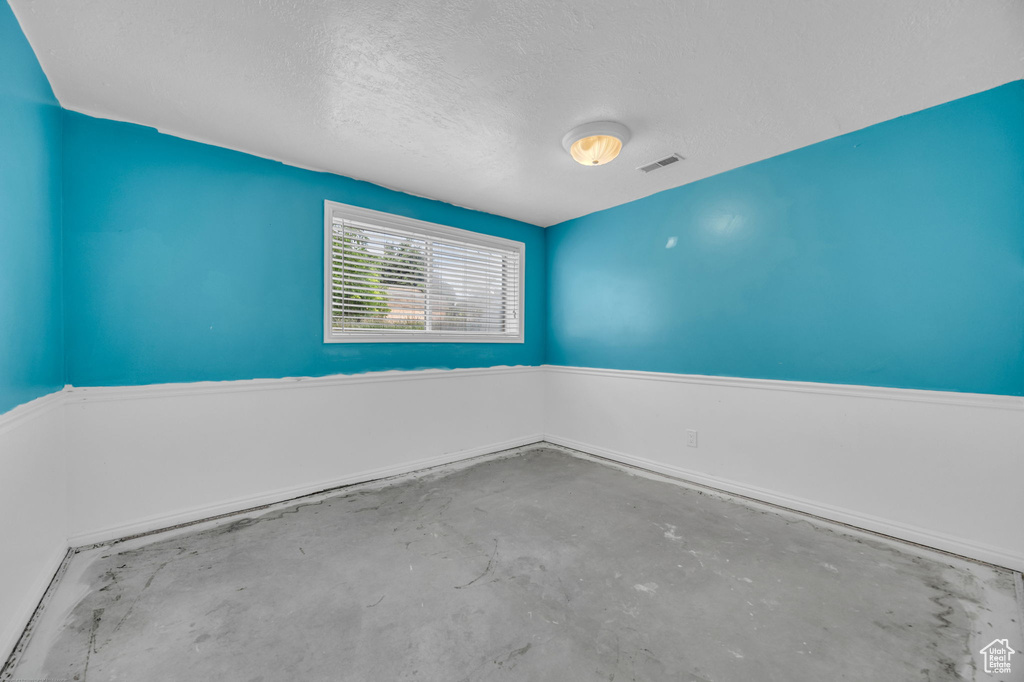 Unfurnished room with unfinished concrete flooring and a textured ceiling