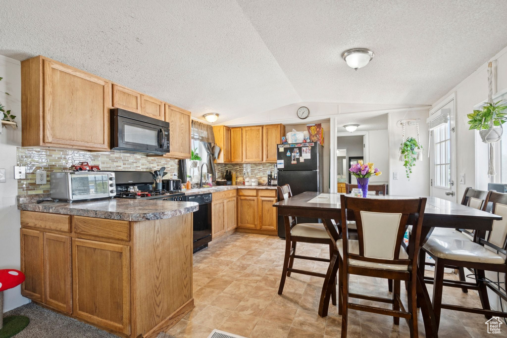 Kitchen with black appliances, decorative backsplash, vaulted ceiling, and a textured ceiling