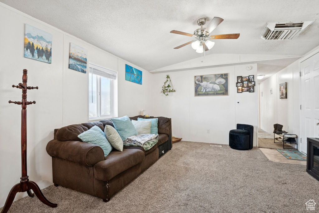 Living room with carpet, vaulted ceiling, a ceiling fan, and a textured ceiling