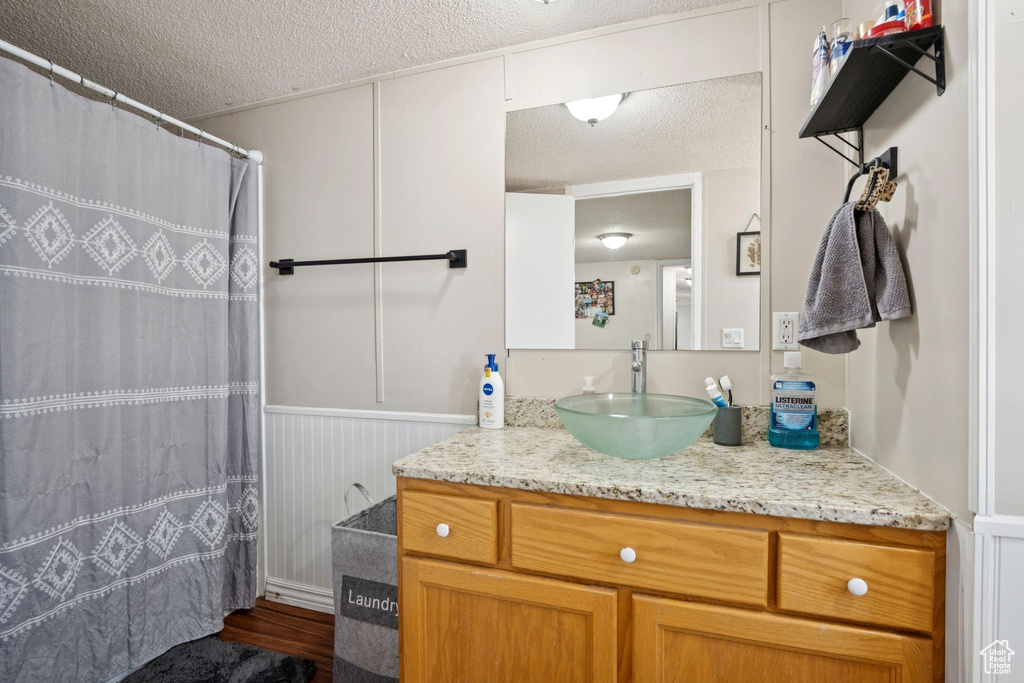 Full bath with a textured ceiling, vanity, a wainscoted wall, wood finished floors, and curtained shower