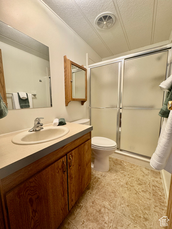 Bathroom featuring vanity, a shower with shower door, a textured ceiling, and tile patterned floors