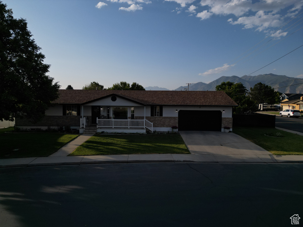 Ranch-style home featuring a porch, a garage, driveway, a mountain view, and a front lawn