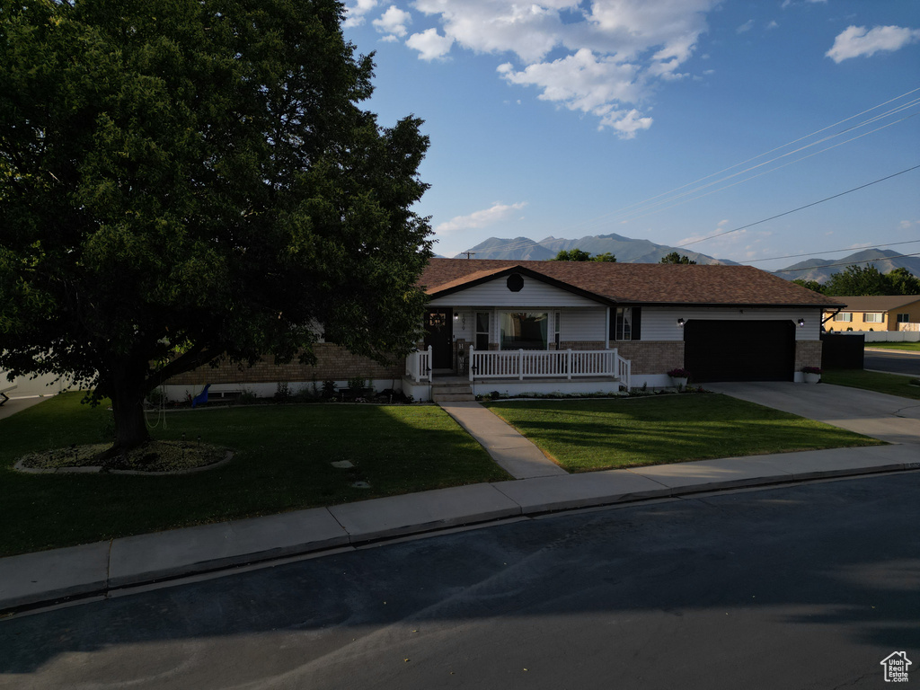 View of front of home featuring a mountain view, a porch, driveway, and a front lawn