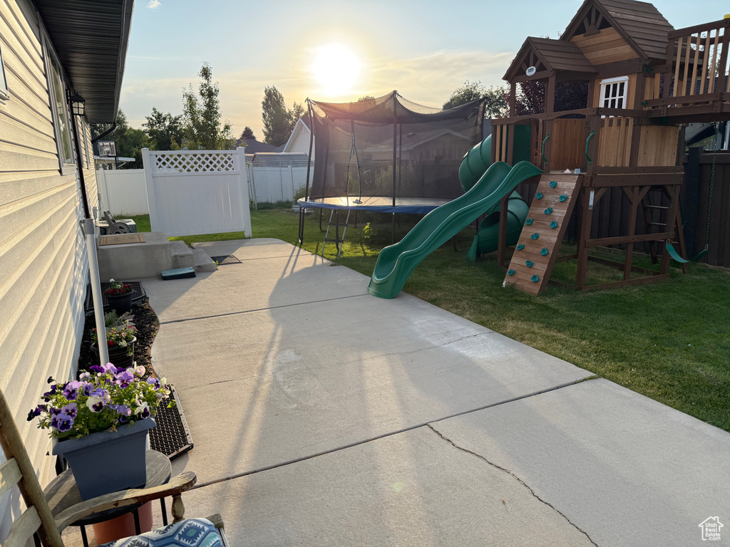 Fenced backyard with a trampoline, a playground, and a patio area
