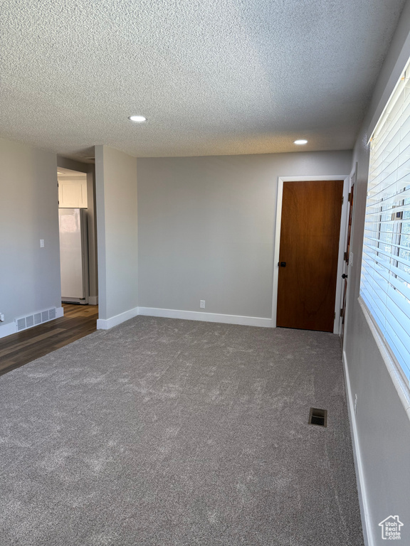 Empty room with dark carpet, a textured ceiling, and recessed lighting