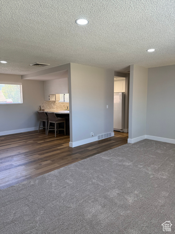 Unfurnished living room with a textured ceiling, dark colored carpet, recessed lighting, and dark wood-type flooring