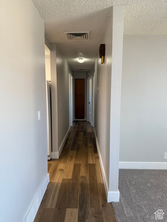 Hall with a textured ceiling and wood finished floors