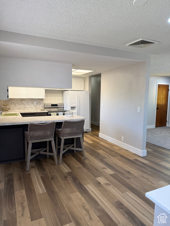 Kitchen with white fridge with ice dispenser, stainless steel electric range, white cabinetry, dark wood-style floors, and a textured ceiling
