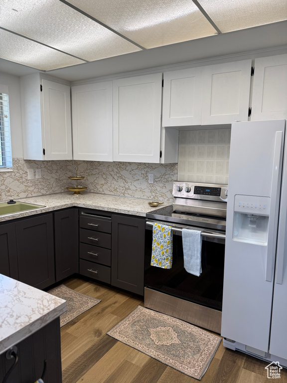 Kitchen with white fridge with ice dispenser, stainless steel range with electric stovetop, white cabinetry, and tasteful backsplash