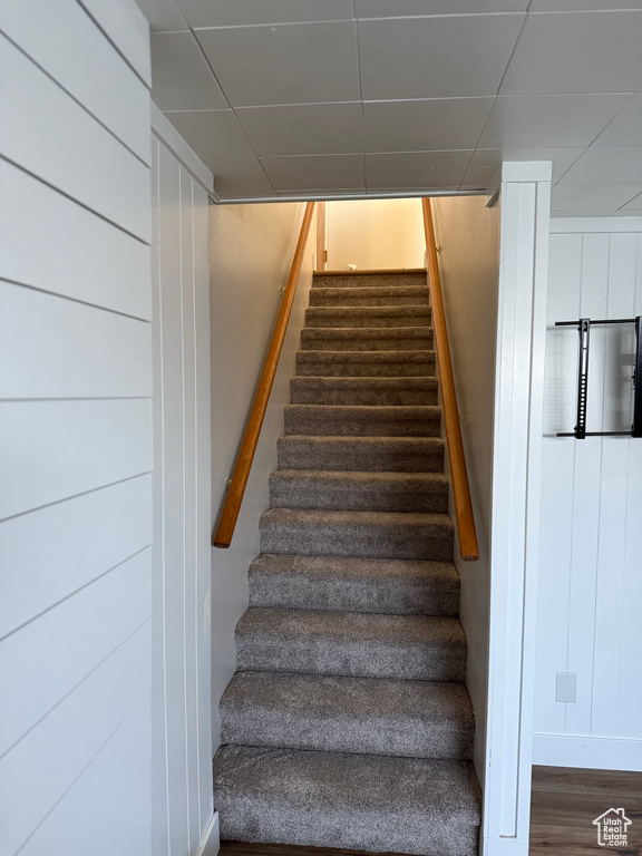 Stairs with wood finished floors and a paneled ceiling