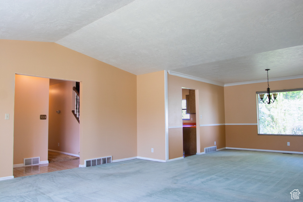 Unfurnished room featuring carpet flooring, a chandelier, a textured ceiling, vaulted ceiling, and ornamental molding