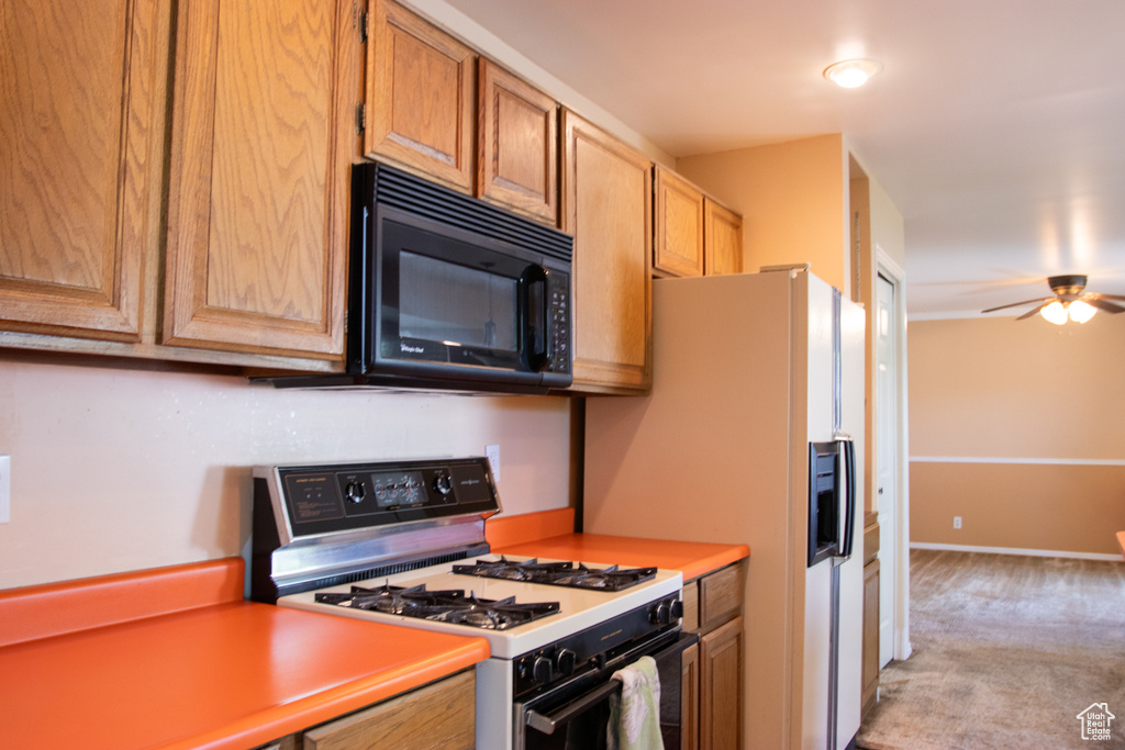 Kitchen with range with gas stovetop, black microwave, a ceiling fan, light carpet, and light countertops