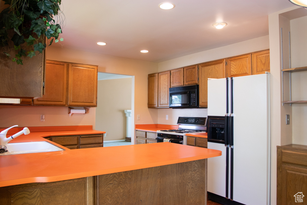 Kitchen featuring black microwave, white refrigerator with ice dispenser, gas range oven, recessed lighting, and light countertops