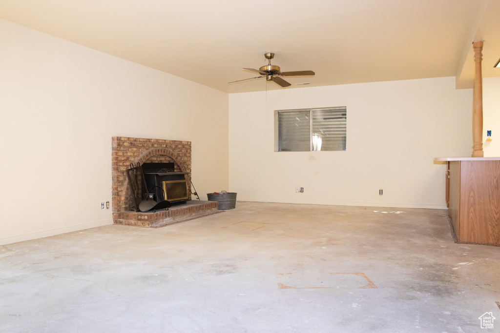 Unfurnished living room featuring a wood stove, a ceiling fan, and concrete floors