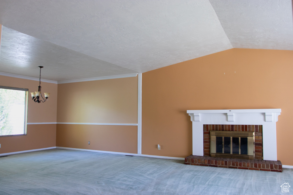 Unfurnished living room with a chandelier, vaulted ceiling, carpet flooring, a textured ceiling, and a brick fireplace