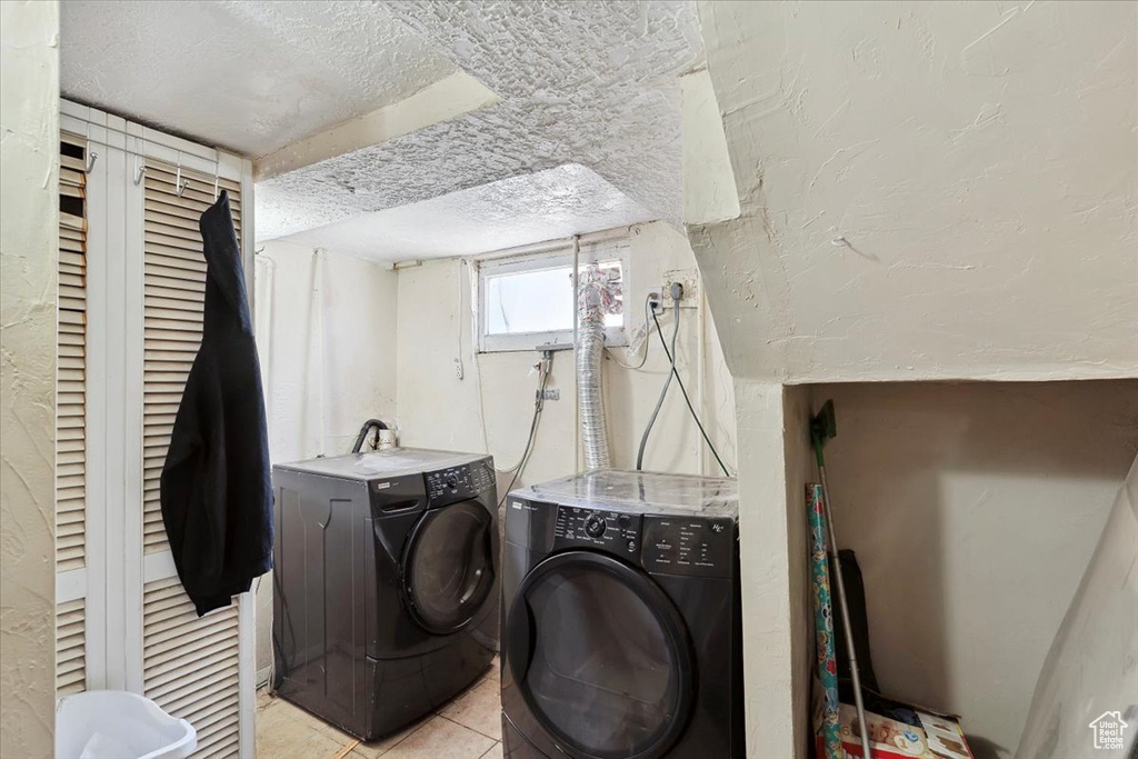 Washroom with a textured ceiling, light tile patterned floors, and separate washer and dryer