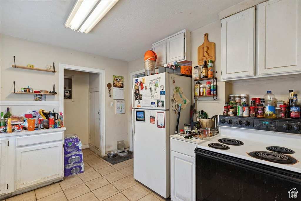 Kitchen featuring electric stove, freestanding refrigerator, light countertops, and white cabinets