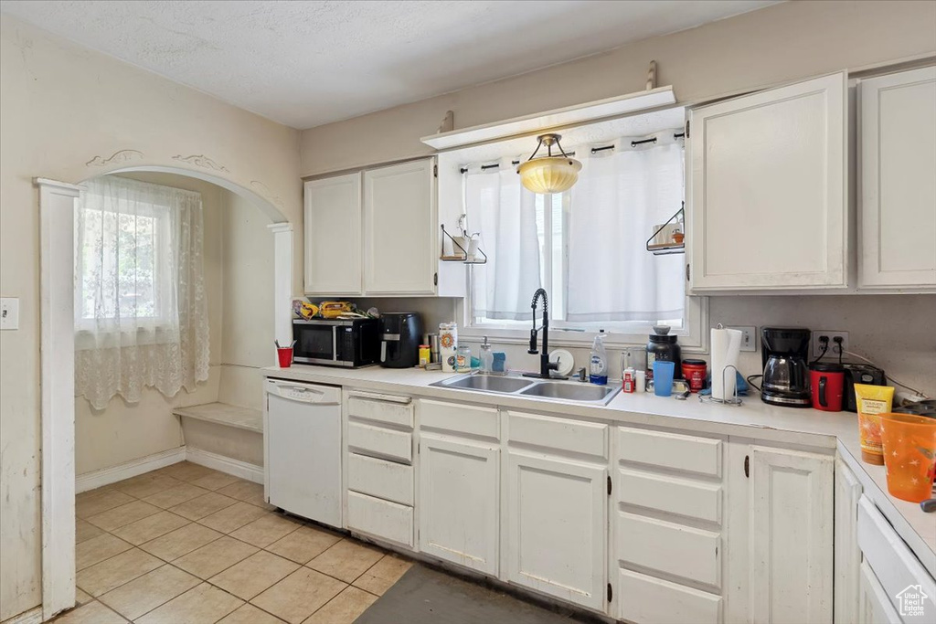 Kitchen with white dishwasher, healthy amount of natural light, light tile patterned floors, and white cabinetry