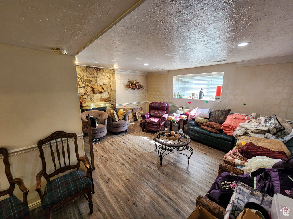 Living room with a textured ceiling, wood-type flooring, crown molding, and a fireplace