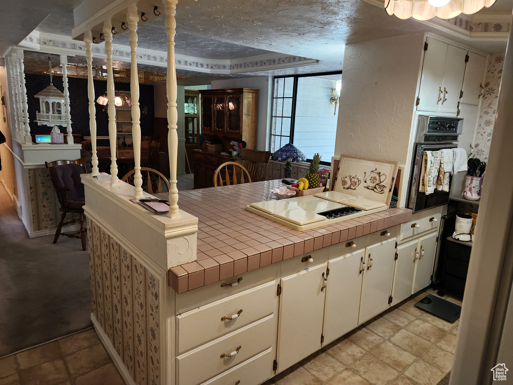Kitchen featuring black oven, stovetop, a peninsula, and tile counters