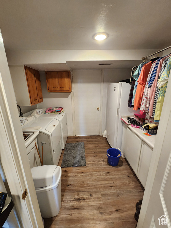 Laundry area with washing machine and clothes dryer, light wood finished floors, and cabinet space