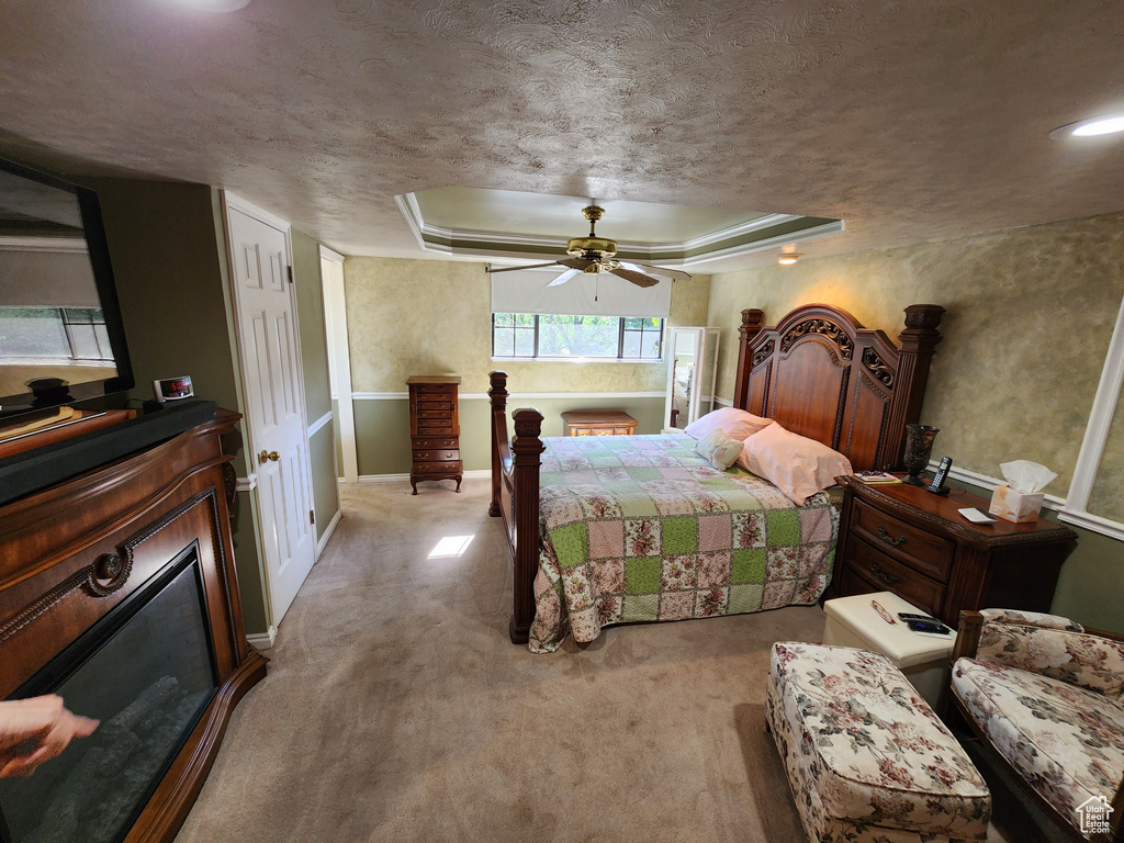 Bedroom with a tray ceiling, light carpet, a textured ceiling, and a ceiling fan