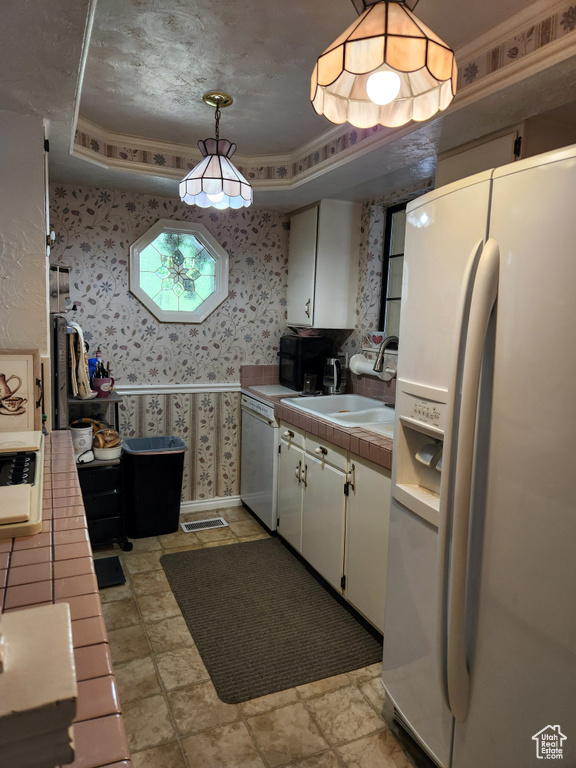 Kitchen featuring white appliances, a tray ceiling, tile countertops, wallpapered walls, and white cabinetry