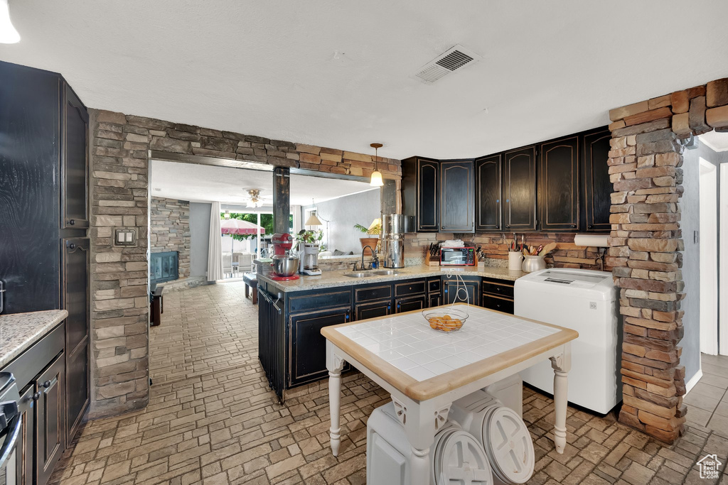 Kitchen featuring brick patterned floors, tile counters, dark brown cabinets, a peninsula, and decorative light fixtures