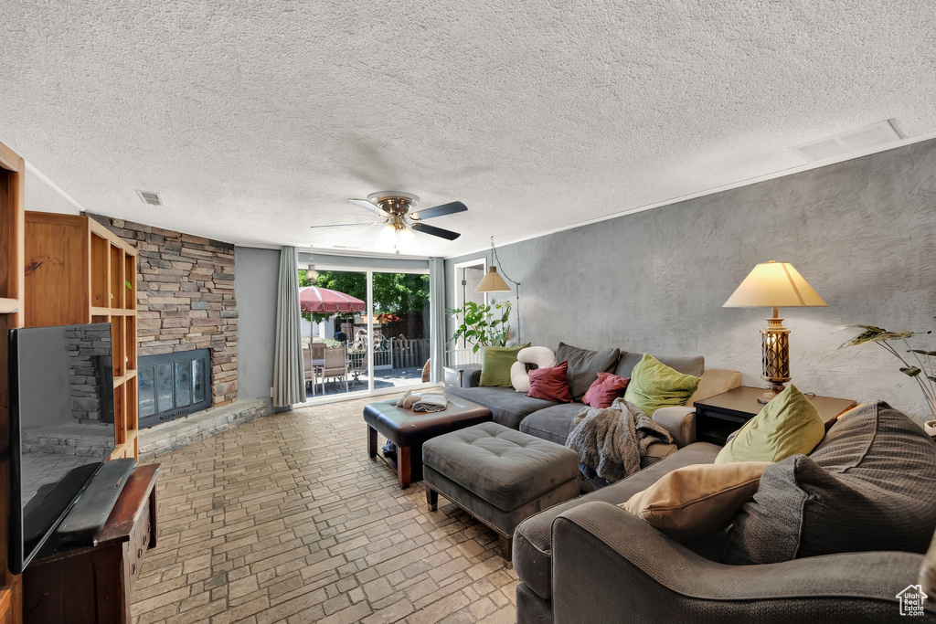 Living area with ceiling fan, brick patterned floors, a fireplace, and a textured ceiling