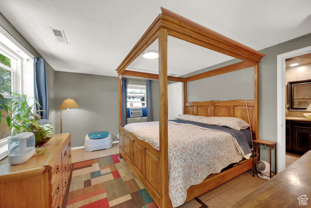 Bedroom featuring light tile patterned flooring, connected bathroom, cooling unit, and a textured ceiling