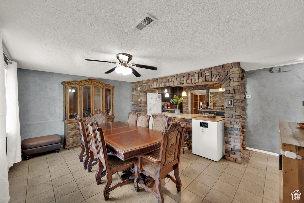 Dining space with light tile patterned floors, a ceiling fan, and a textured ceiling