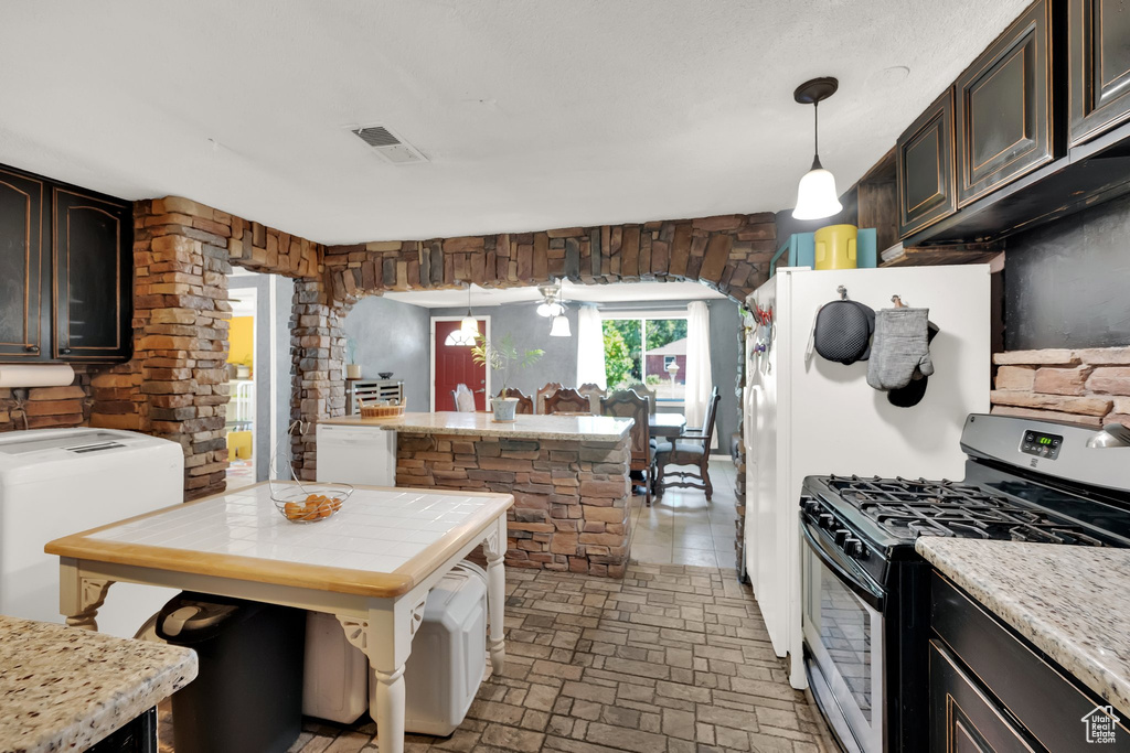Kitchen featuring gas range, dark brown cabinetry, hanging light fixtures, and arched walkways