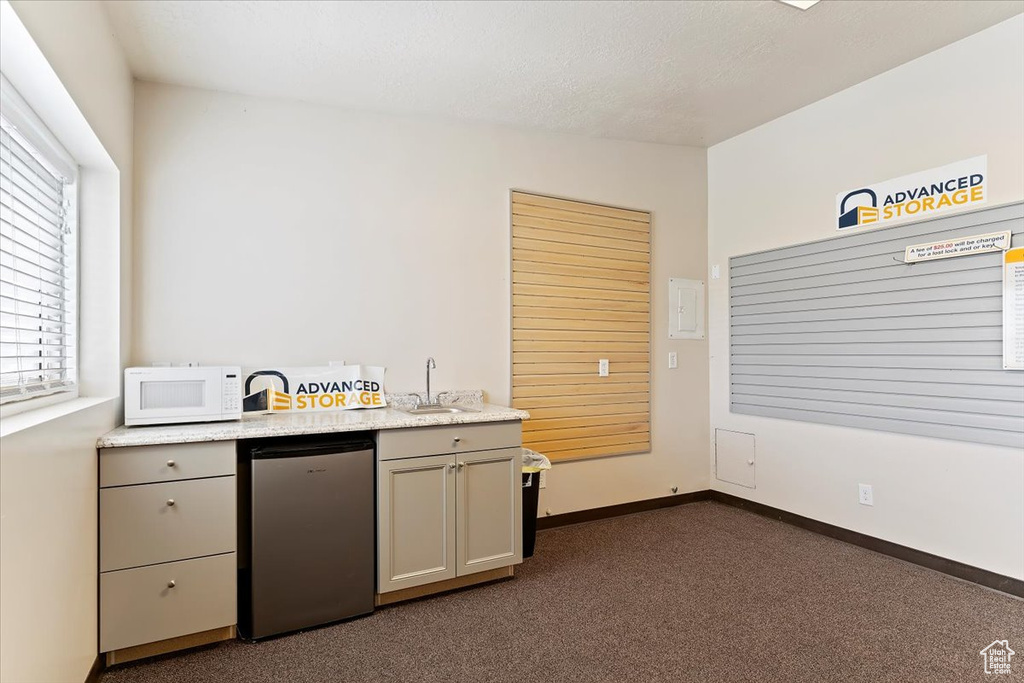 Kitchen featuring white microwave, refrigerator, dark carpet, and gray cabinets