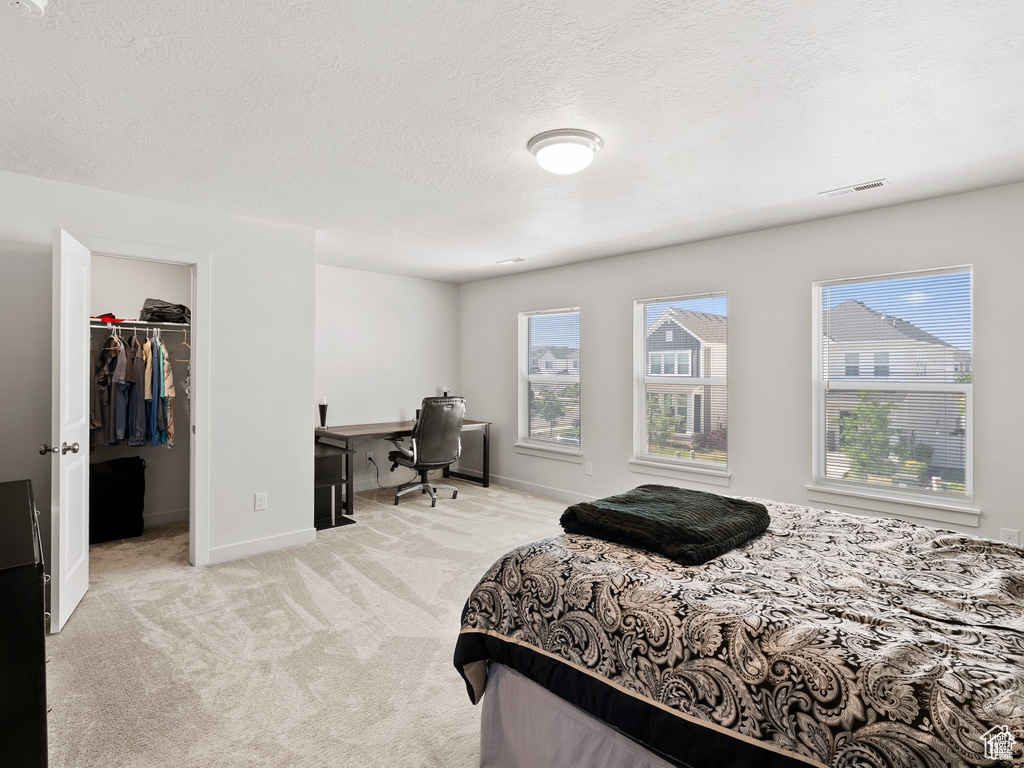 Bedroom with carpet, an office area, a walk in closet, and a textured ceiling