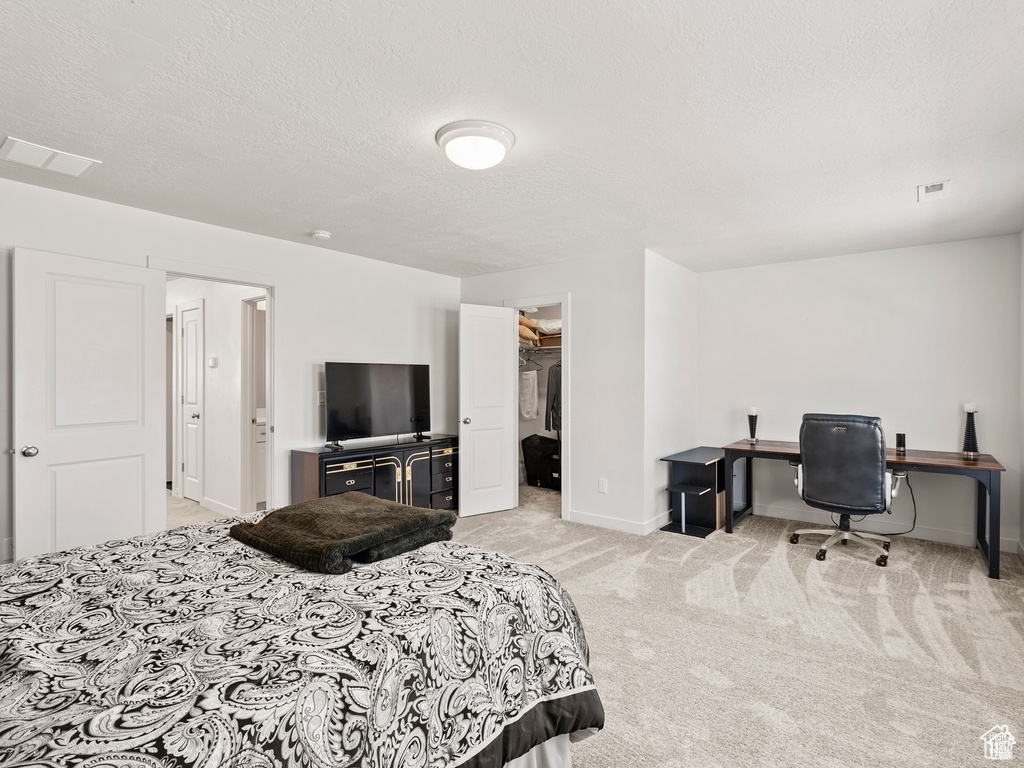 Bedroom with light carpet, a textured ceiling, a spacious closet, and a desk