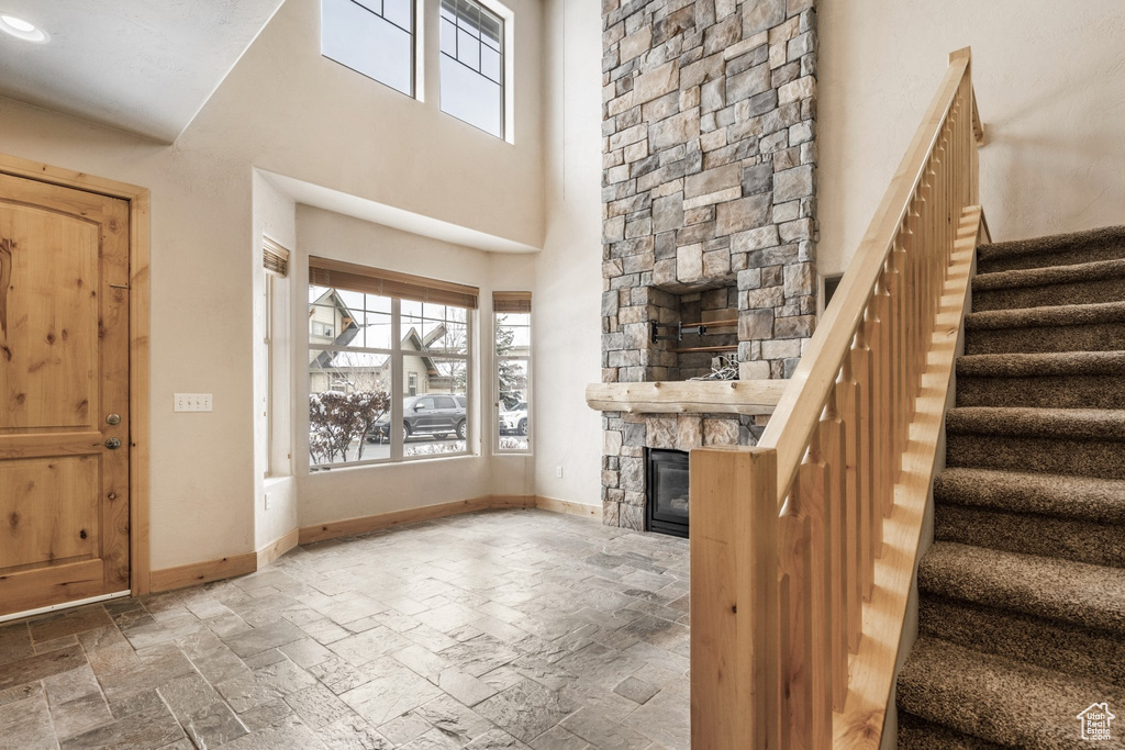 Foyer entrance with stone tile flooring, a stone fireplace, stairway, and a towering ceiling