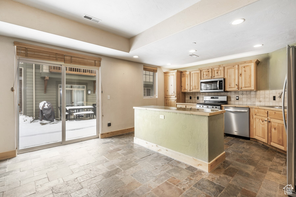 Kitchen with stainless steel appliances, stone tile floors, a kitchen island, recessed lighting, and backsplash
