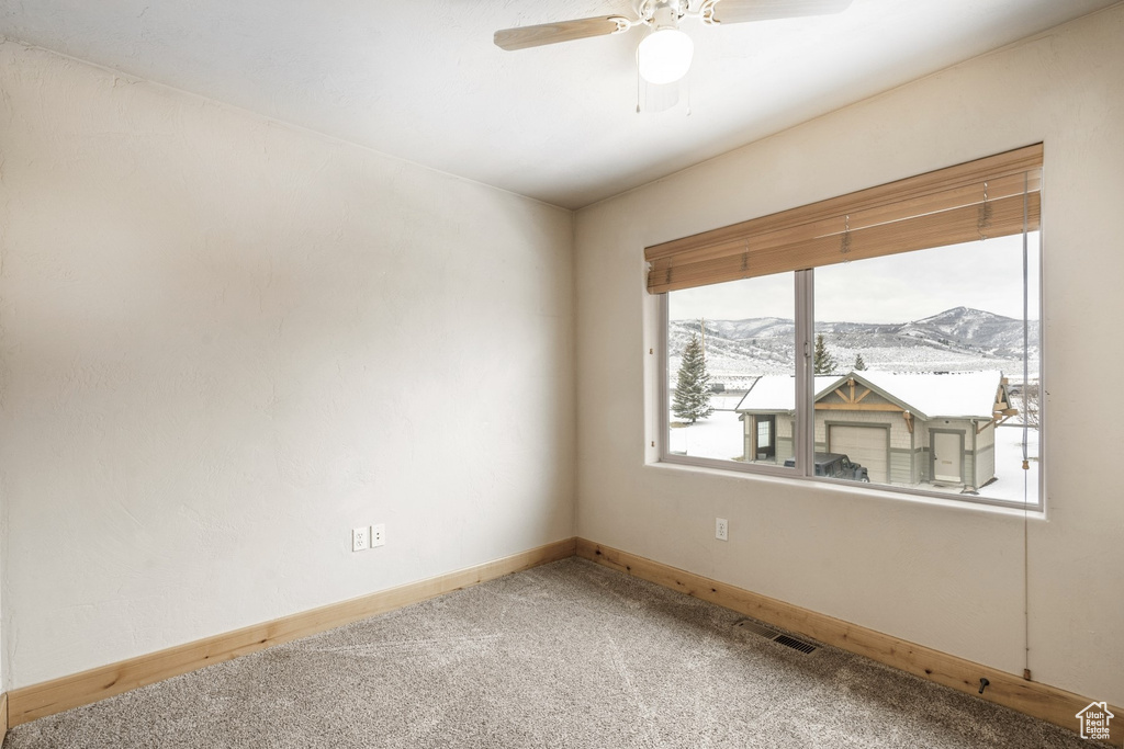 Carpeted empty room featuring a mountain view and ceiling fan