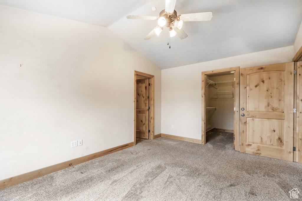 Unfurnished bedroom featuring vaulted ceiling, carpet flooring, a walk in closet, a closet, and a ceiling fan