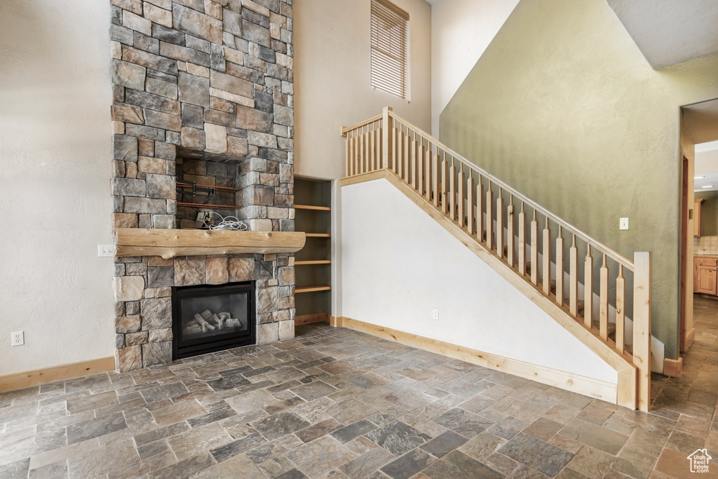 Unfurnished living room with stone tile flooring, stairway, and a stone fireplace