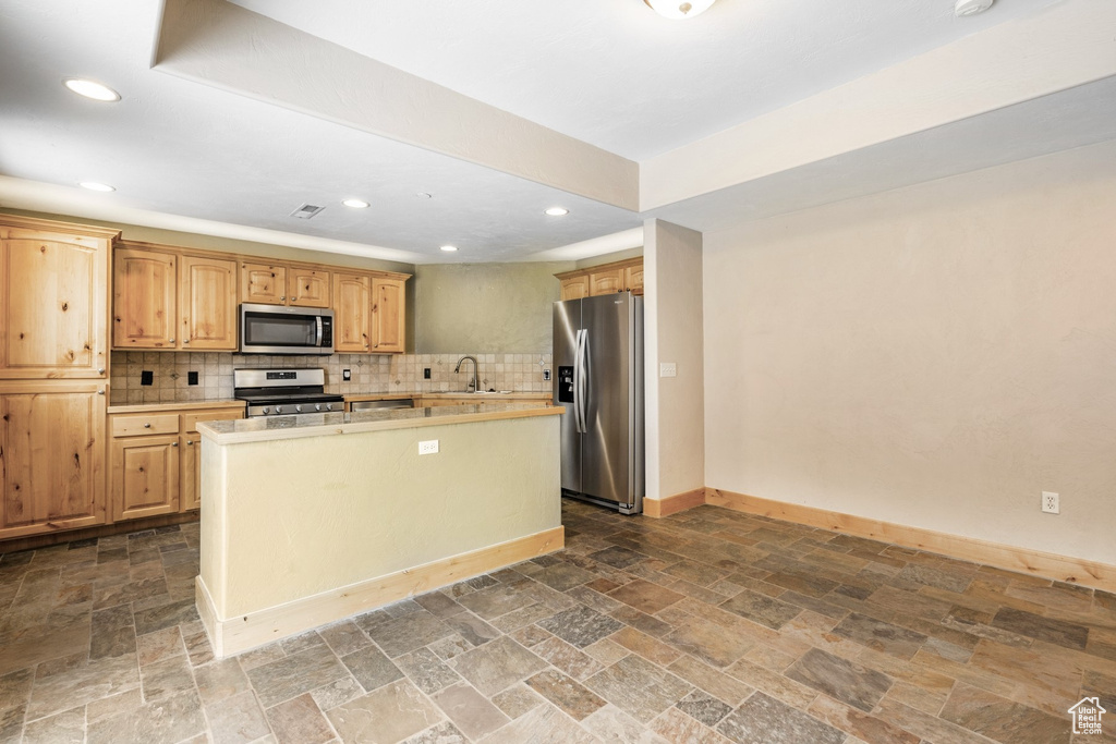 Kitchen with appliances with stainless steel finishes, stone tile flooring, light countertops, tasteful backsplash, and recessed lighting