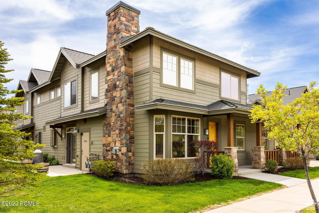 View of front of home with covered porch, a front yard, a chimney, and a shingled roof