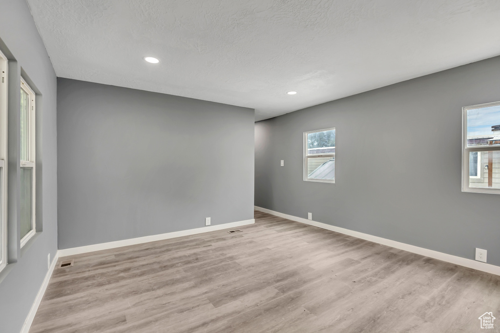 Empty room featuring wood finished floors, plenty of natural light, a textured ceiling, and recessed lighting