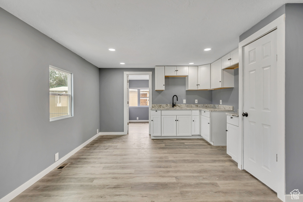 Kitchen with recessed lighting, white cabinetry, light stone counters, and light wood-style floors