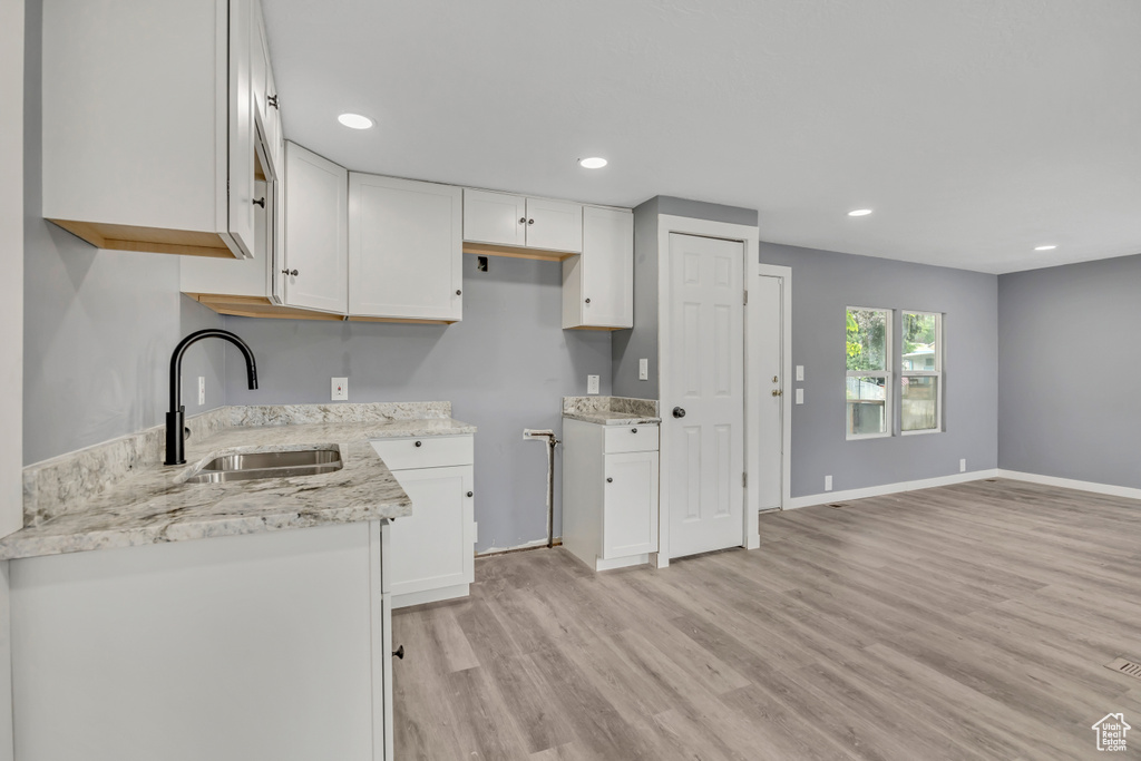 Kitchen featuring light wood finished floors, white cabinets, light stone countertops, recessed lighting, and open floor plan