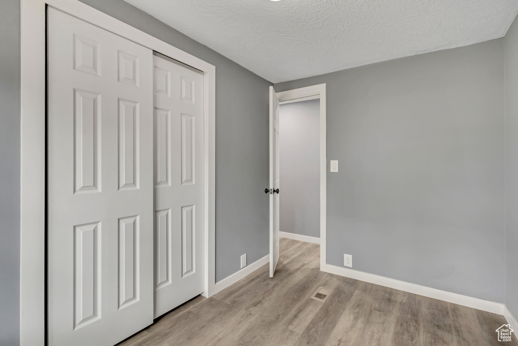 Unfurnished bedroom featuring light wood-style flooring, a textured ceiling, and a closet