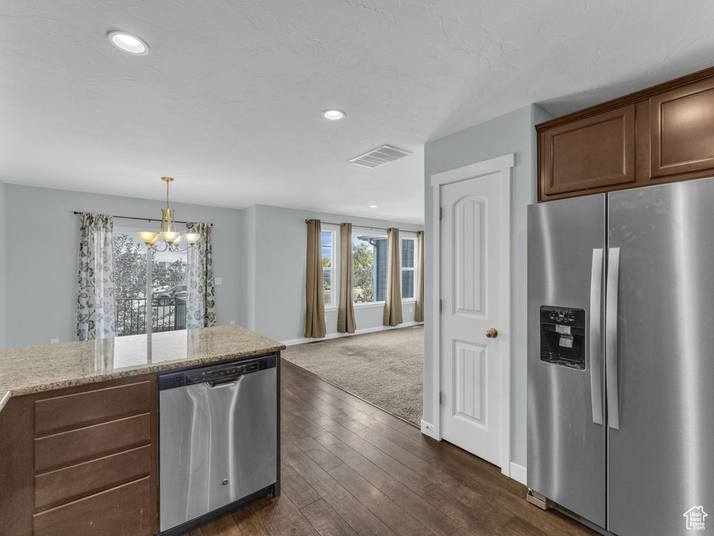 Kitchen with appliances with stainless steel finishes, a chandelier, dark wood-style flooring, recessed lighting, and light stone countertops