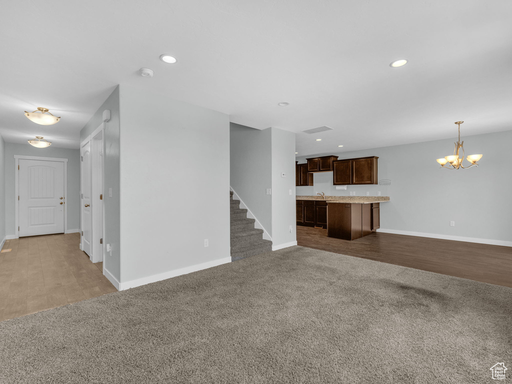Unfurnished living room featuring a chandelier, carpet flooring, recessed lighting, stairs, and wood finished floors