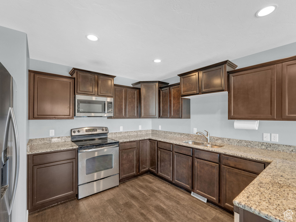Kitchen featuring appliances with stainless steel finishes, dark wood-style flooring, dark brown cabinets, recessed lighting, and light stone countertops